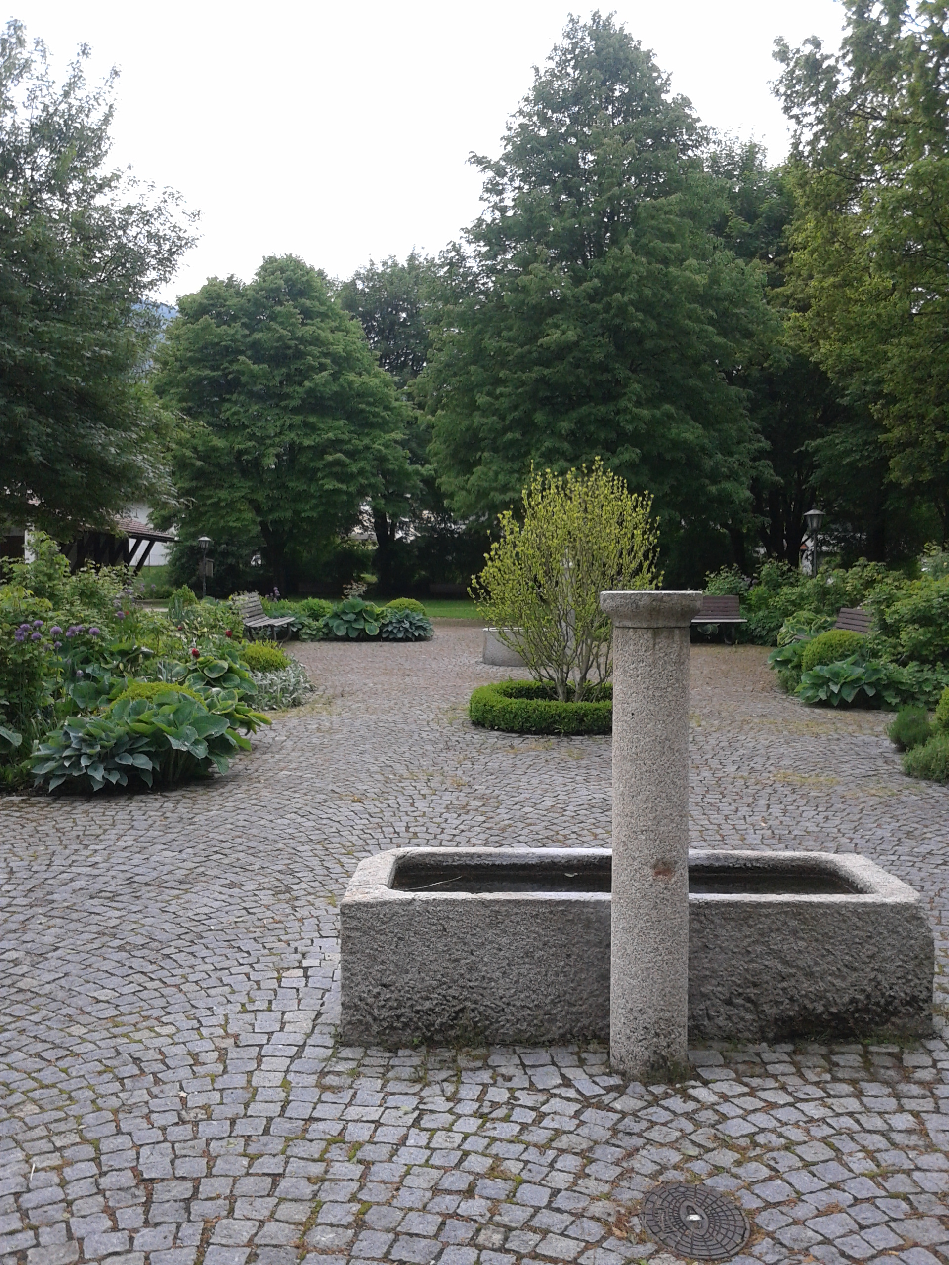 Hier zeigt sich ein anderer, rechteckiger Brunnen des Parkes. Auch dieser wird von Bäumen umrahmt.